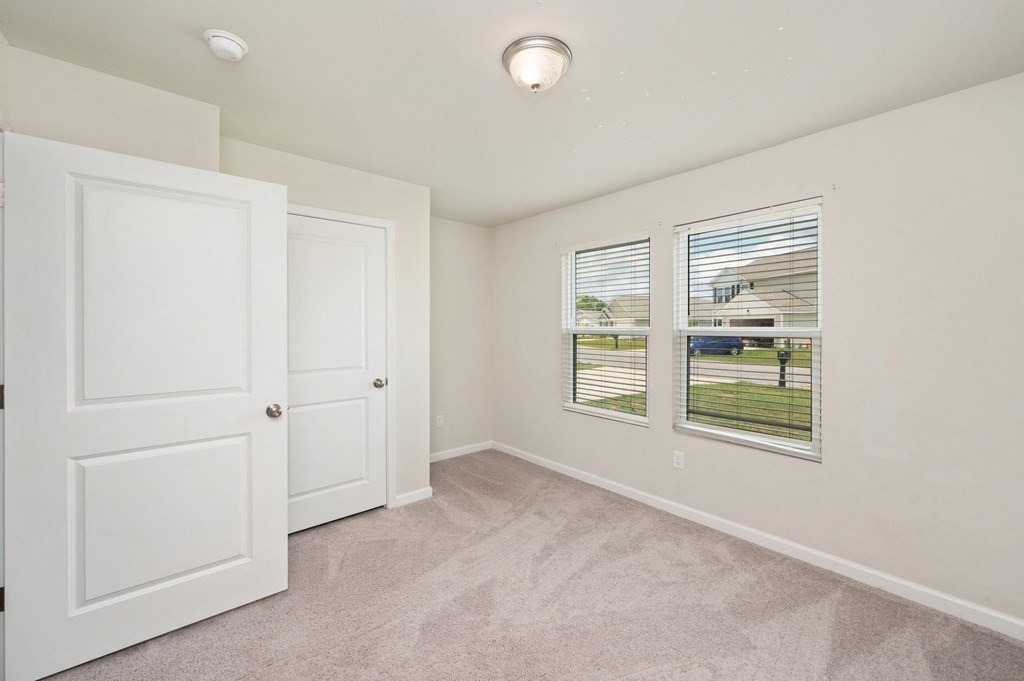 an empty bedroom with two windows and a door