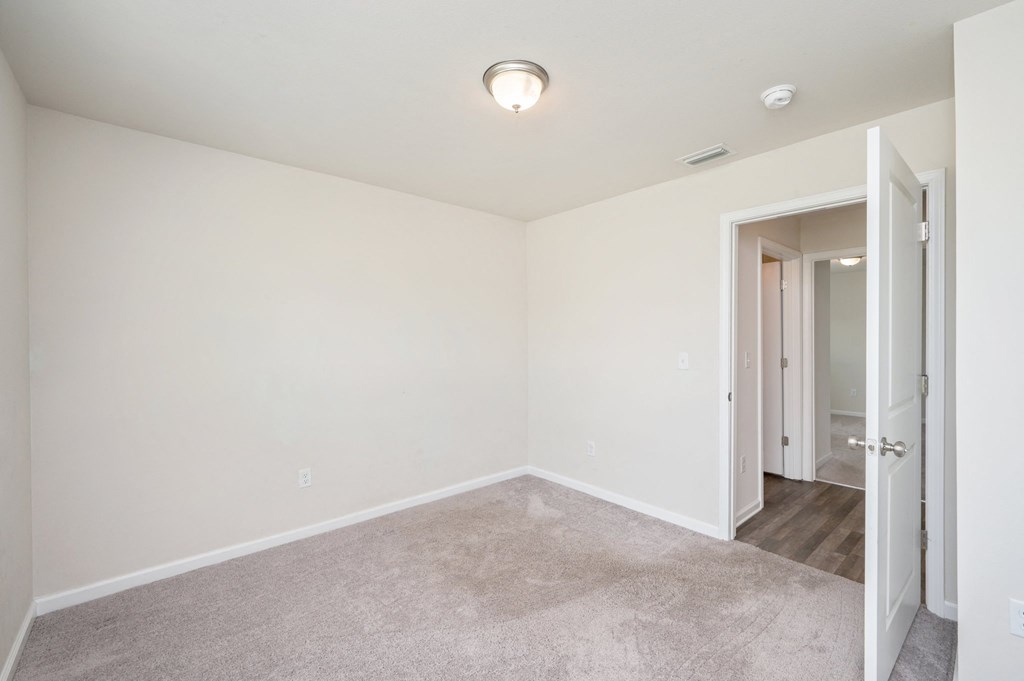 a bedroom with white walls and carpet and a door to a hallway