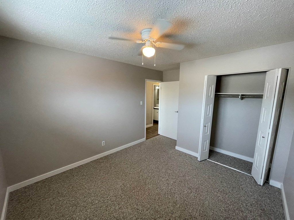 an empty living room with a ceiling fan and a closet