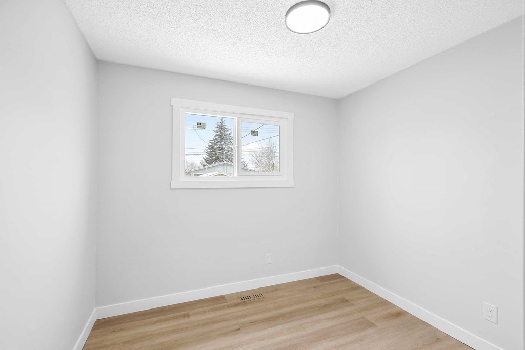 a bedroom with white walls and a window and a hardwood floor