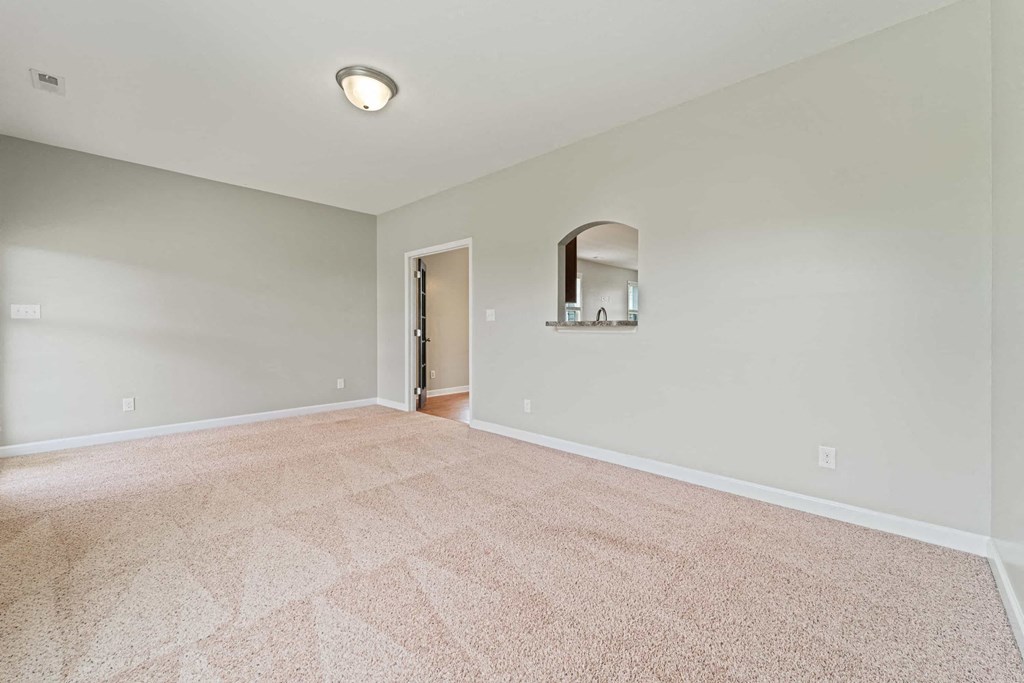 a spacious living room with carpet and a door to a hallway