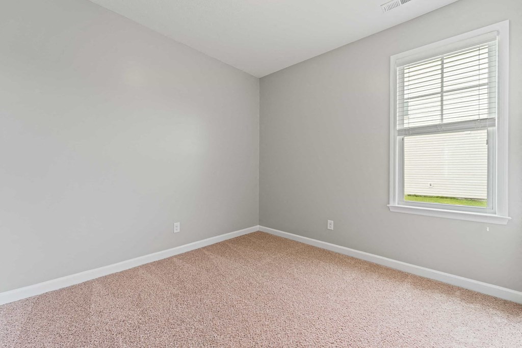an empty bedroom with a window and carpet