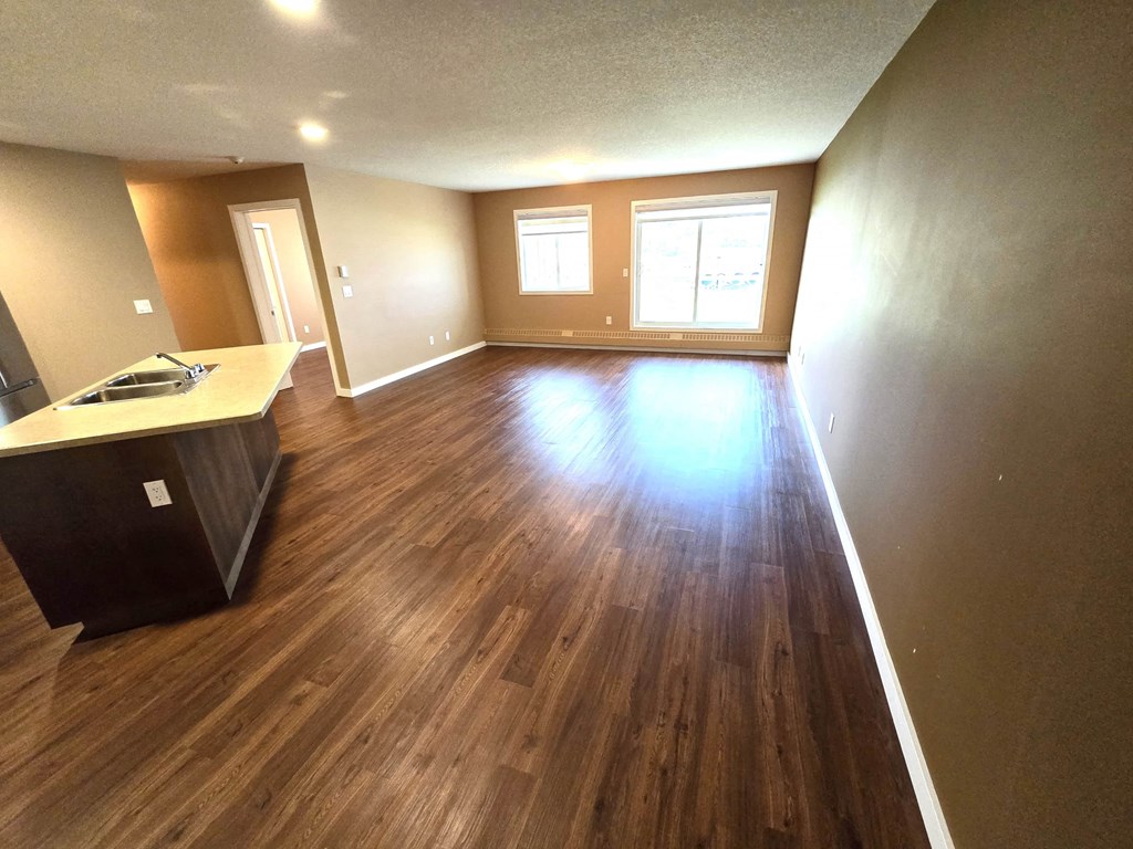 an empty living room with wooden floors and a kitchen