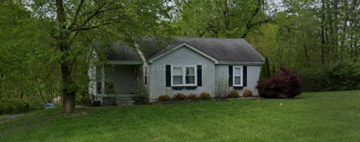 a small gray house with a green lawn and trees