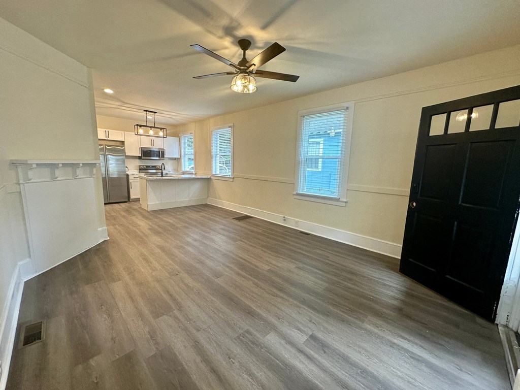 an empty living room with a ceiling fan and a kitchen