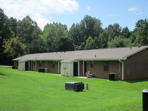 the front of a brick building with a grass field and trees