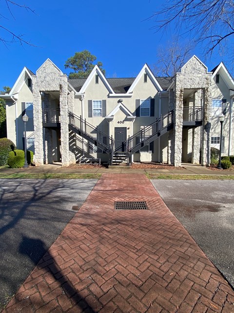 A brick pathway leads to a large, two-story residential building with a balcony on the second floor.