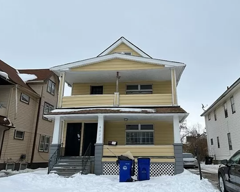 a yellow house with two trash cans in the snow