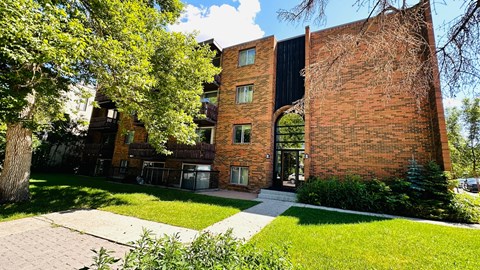 A red brick building with a black roof and a tree in front of it.