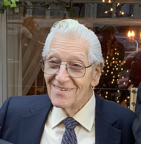 A man with white hair and glasses is wearing a suit and tie.