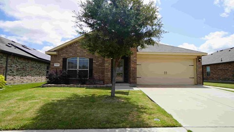 the front of a brick house with a sidewalk and a tree