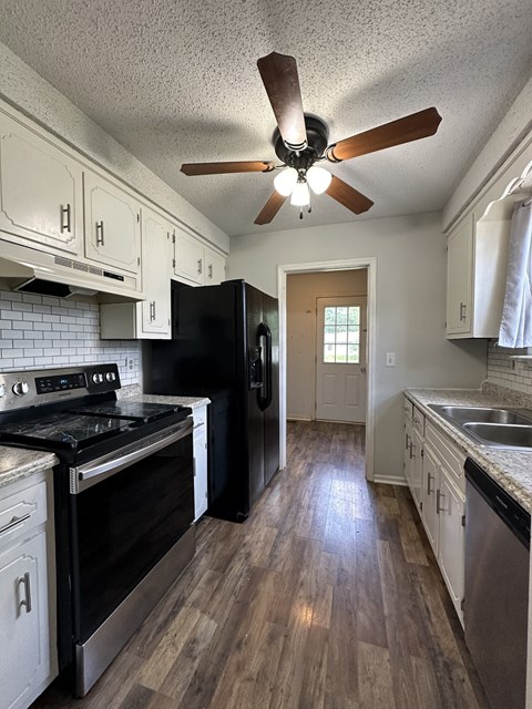 a kitchen with white cabinets and black appliances and a ceiling fan