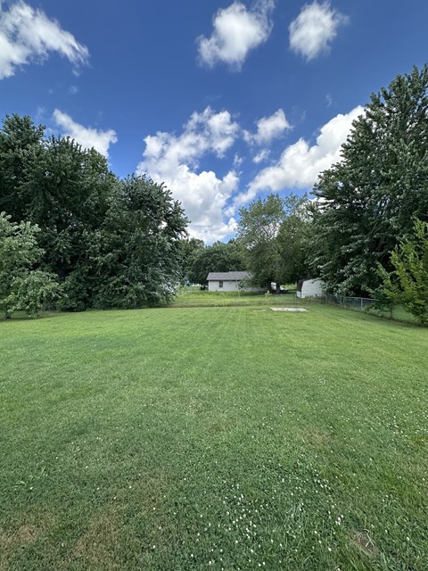 a large grassy field with trees and a house in the background
