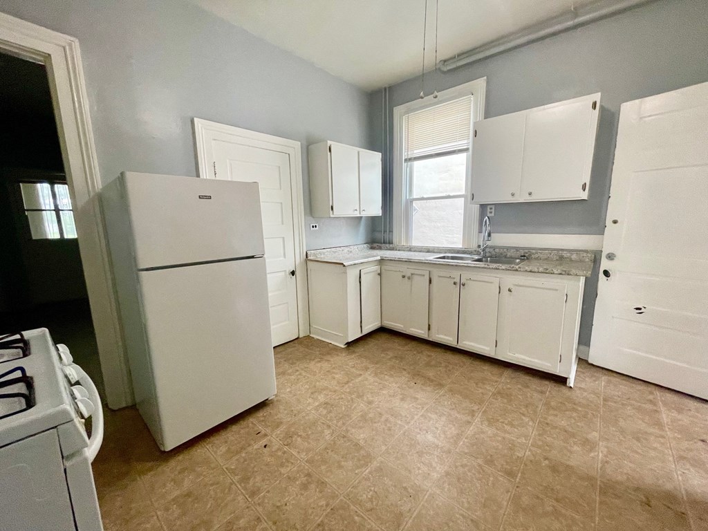 an empty kitchen with white cabinets and a refrigerator