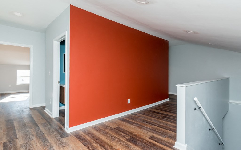 a red wall in a room with wood floors and a staircase