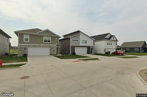 A row of houses with a red car parked in the driveway of the second house from the left.