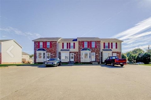 A red brick building with white doors and windows is surrounded by a parking lot.
