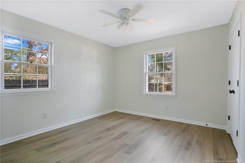 an empty bedroom with a ceiling fan and two windows