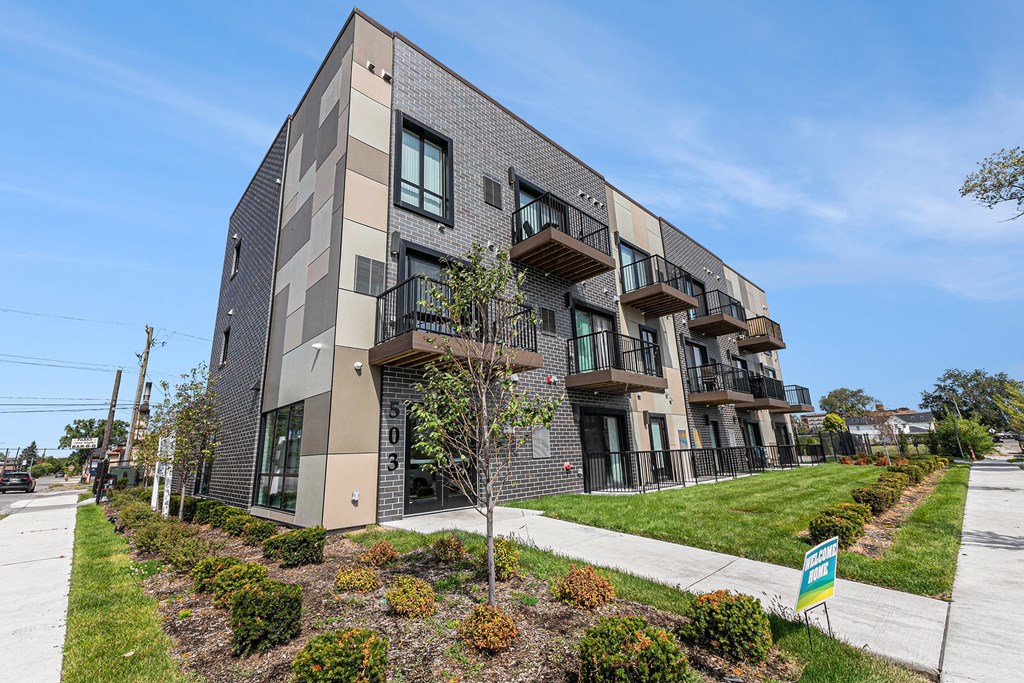 A modern apartment building with balconies and a green lawn in front.