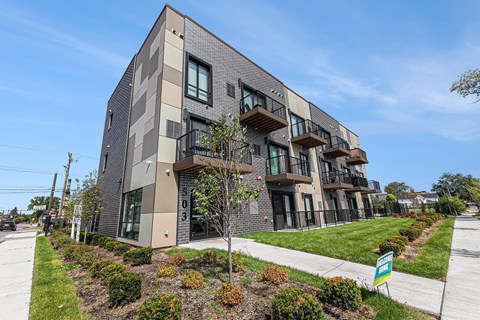 A modern apartment building with balconies and a green lawn in front.