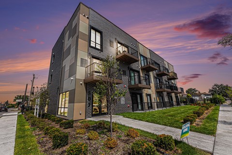 A modern apartment building with balconies and a small garden in front.