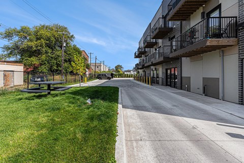 A sunny day on a quiet street with apartment buildings on one side and a picnic table on the other.