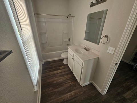 A white bathroom with wood floors and a white toilet.
