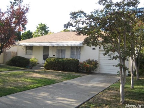 A white house with a brown roof and a tree in front.
