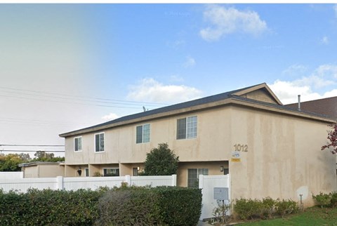 a tan house with a white fence and bushes