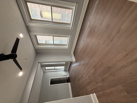 A ceiling fan is on the left side of a room with wooden walls and ceiling.