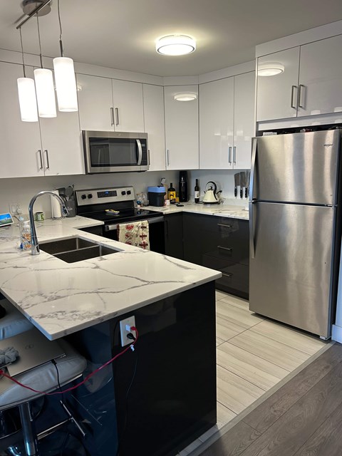A kitchen with a stainless steel refrigerator and black countertops.