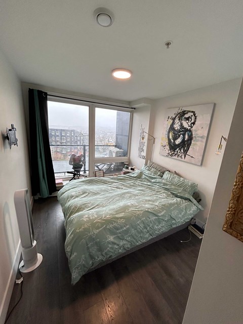 A bedroom with a bed, a window with a view, and a painting on the wall.