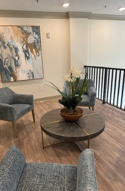 A living room with a grey sofa, a grey armchair, a round coffee table with a plant and a painting in the background.