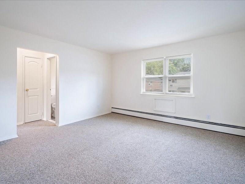 A room with a carpeted floor, a window, and a door.
