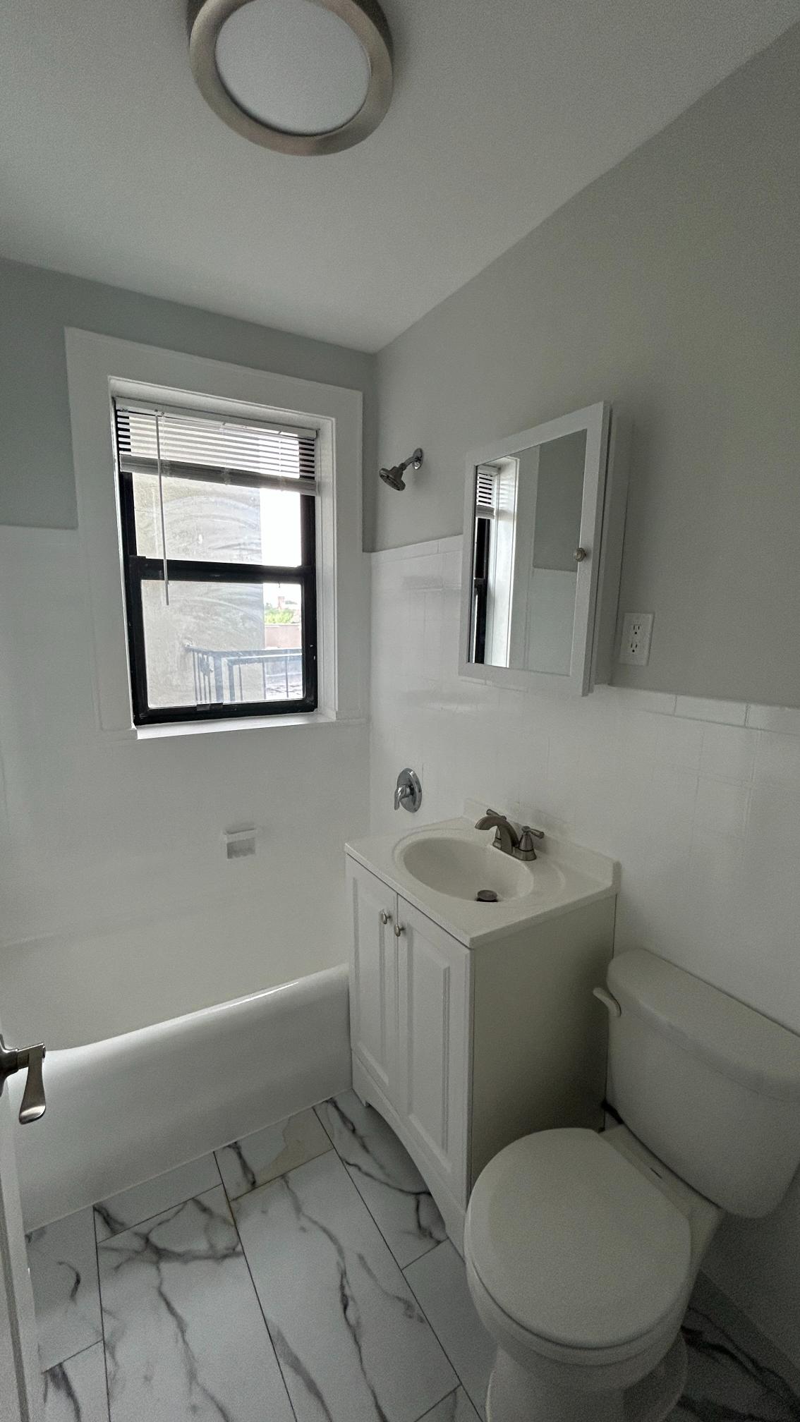 A white toilet sits in a bathroom with a marble floor and a window.