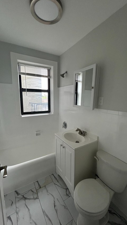 A white toilet sits in a bathroom with a marble floor and a window.