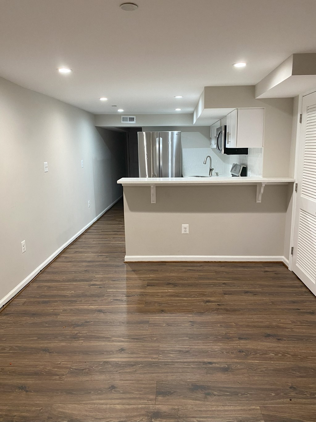 an empty living room with wood floors and a kitchen