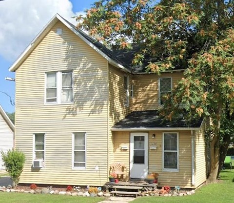 A yellow house with a black roof and a white door.