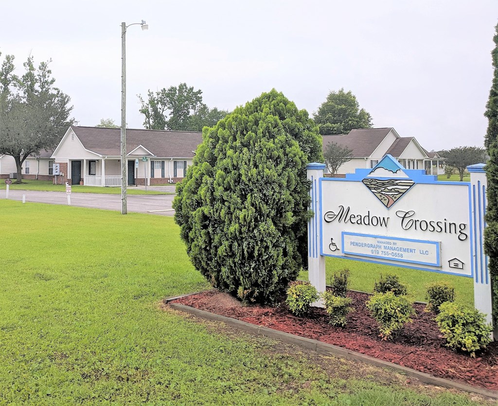 a sign for meadow crossing with a house in the background