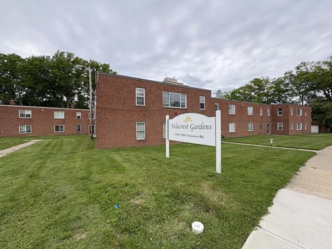 A sign for "Nolacrest Gardens" stands in front of a brick building.