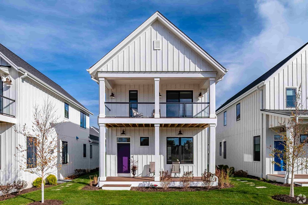 A white house with a purple door is surrounded by other white houses.