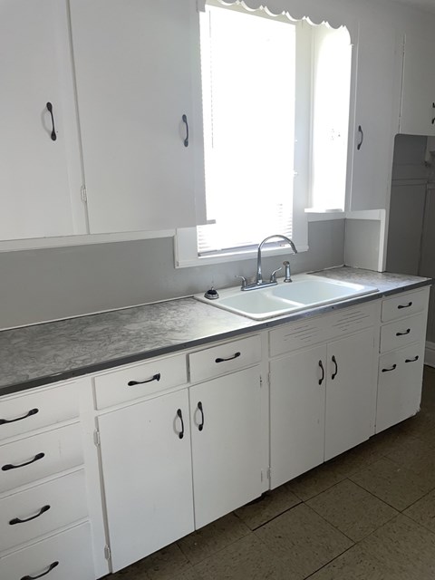A kitchen with white cabinets and a sink under a window.