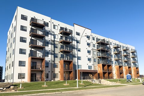 A large white apartment building with balconies and a blue sky in the background.