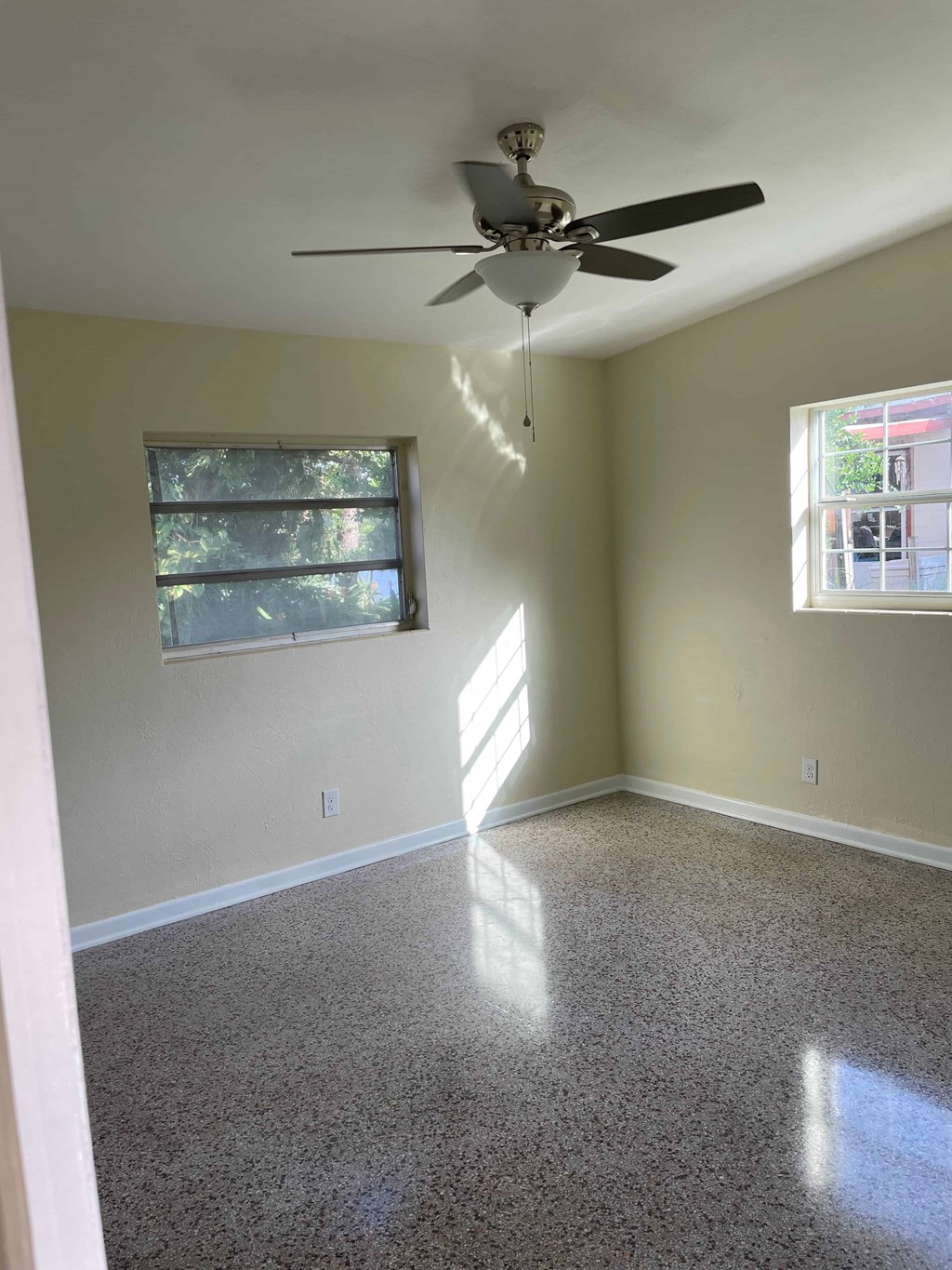 A room with a ceiling fan and two windows.