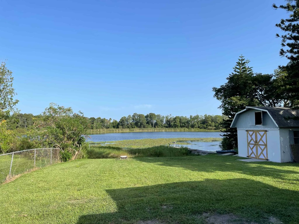A shed sits in a grassy field next to a lake.