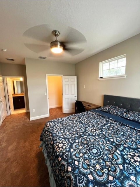 A bedroom with a patterned bedspread and a ceiling fan.