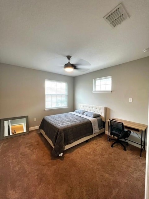 A bedroom with a bed, desk, and fan.
