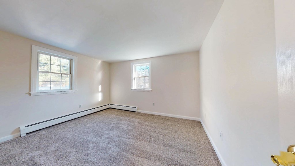 A room with carpeted floor and two windows.