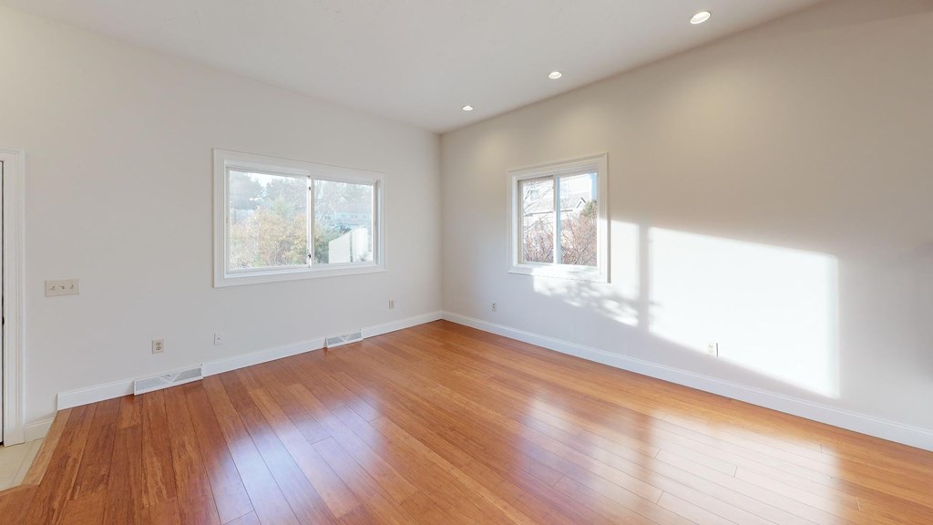A room with wooden floors and two windows letting in sunlight.