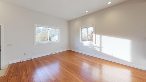 A room with wooden floors and two windows letting in sunlight.